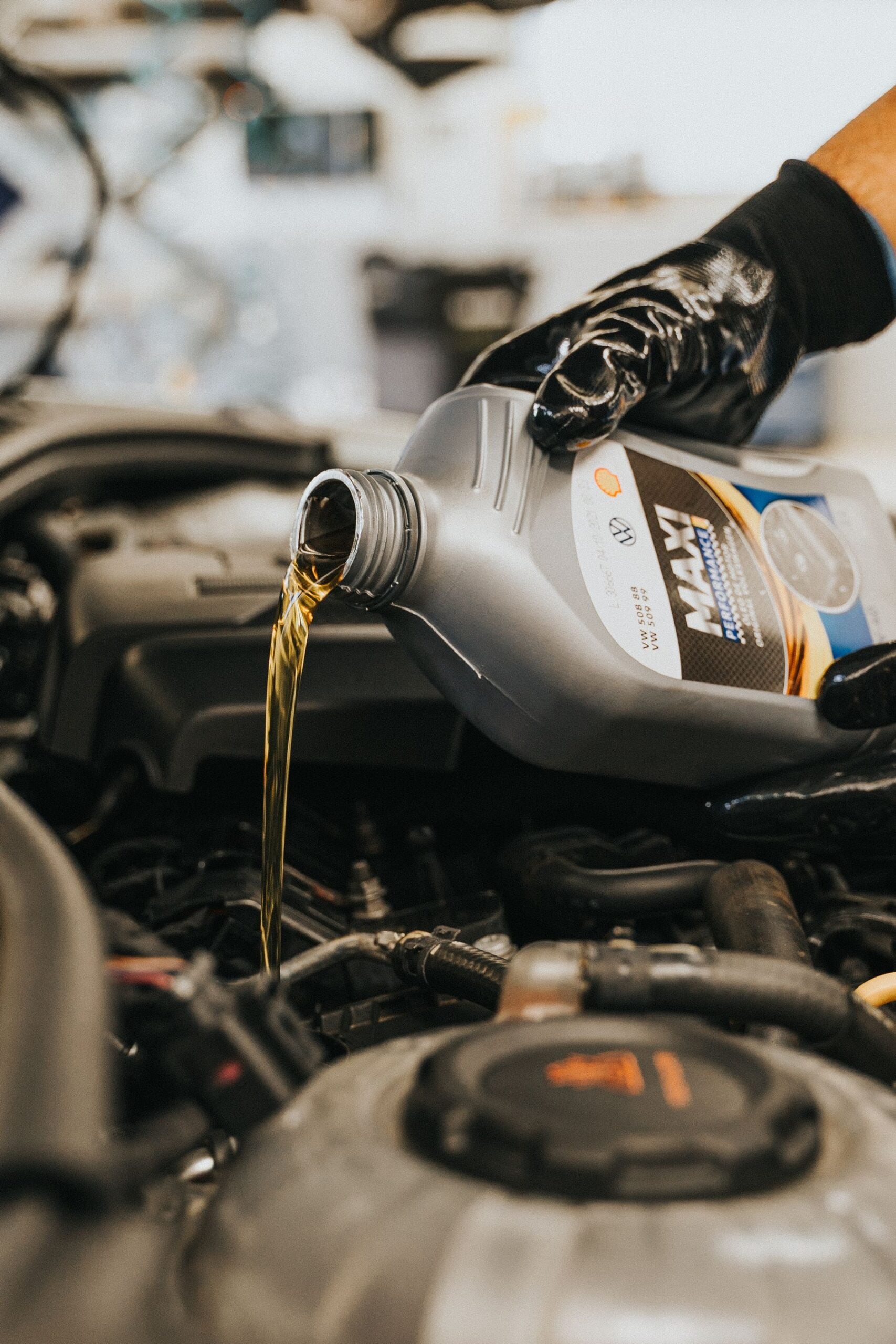 Technician adding motor oil beneath the hood of a vehicle